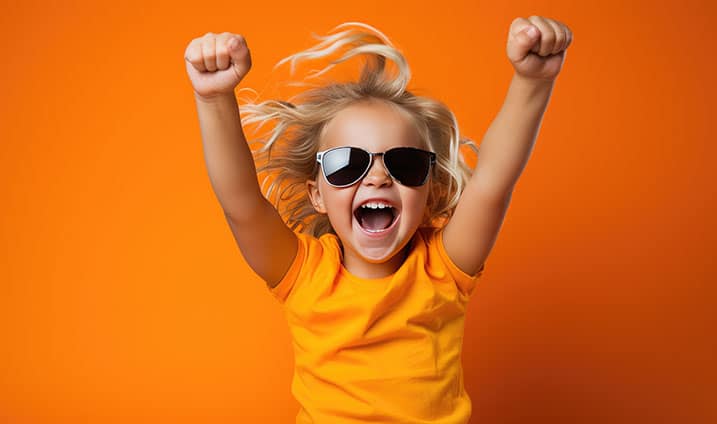 Small child shouts loudly while raising hands up in victory against isolated bright orange background.